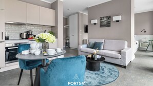 A modern living room with a grey sofa, a coffee table, and a dining area with a table and chairs. There is a kitchen in the background with cabinets and a stove. - "Arriving" in the heart of St. Peter-Ording (Sankt Peter-Ording)