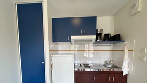 A compact kitchen with a white refrigerator, a stove, and a sink. There are blue cabinets above the stove and a towel hanging on the wall. - T2 Apartment with Balcony and Shared Pool, Near Spa (La Roche-Posay)