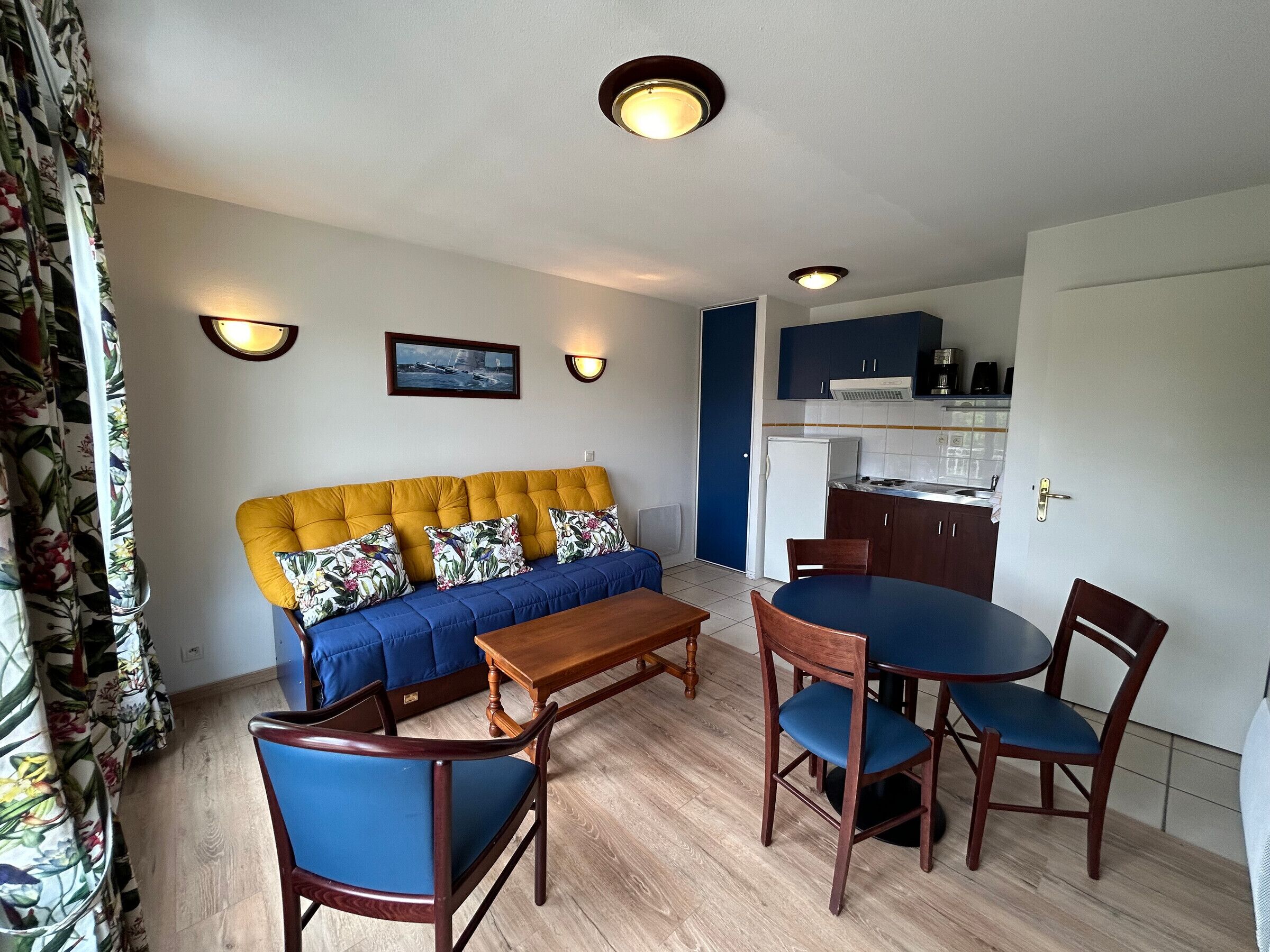 A living room with a sofa, chairs, a coffee table, and a kitchen area with cabinets and a refrigerator.