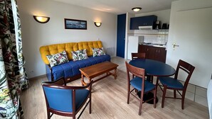 A living room with a sofa, chairs, a coffee table, and a kitchen area with cabinets and a refrigerator. - T2 Apartment with Balcony and Shared Pool, Near Spa (La Roche-Posay)