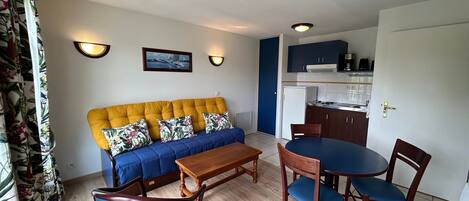 A living room with a sofa, chairs, a coffee table, and a kitchen area with cabinets and a refrigerator.