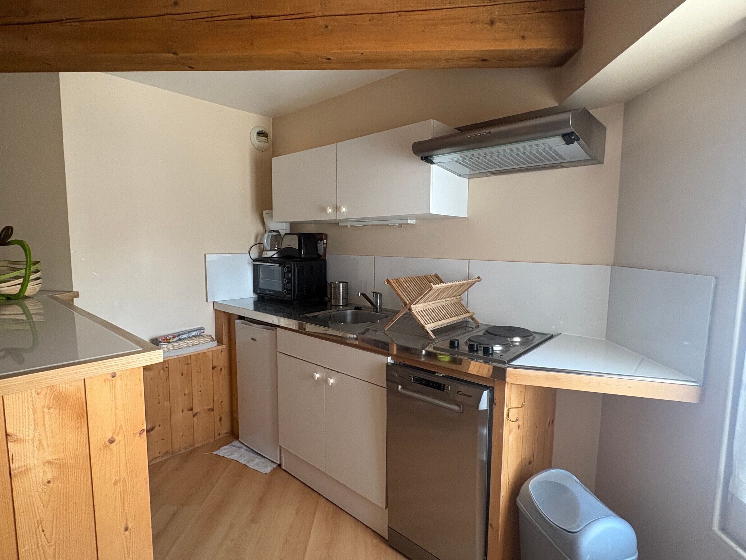 A compact kitchen with a dishwasher, a stove, a microwave, and a hanging rack.