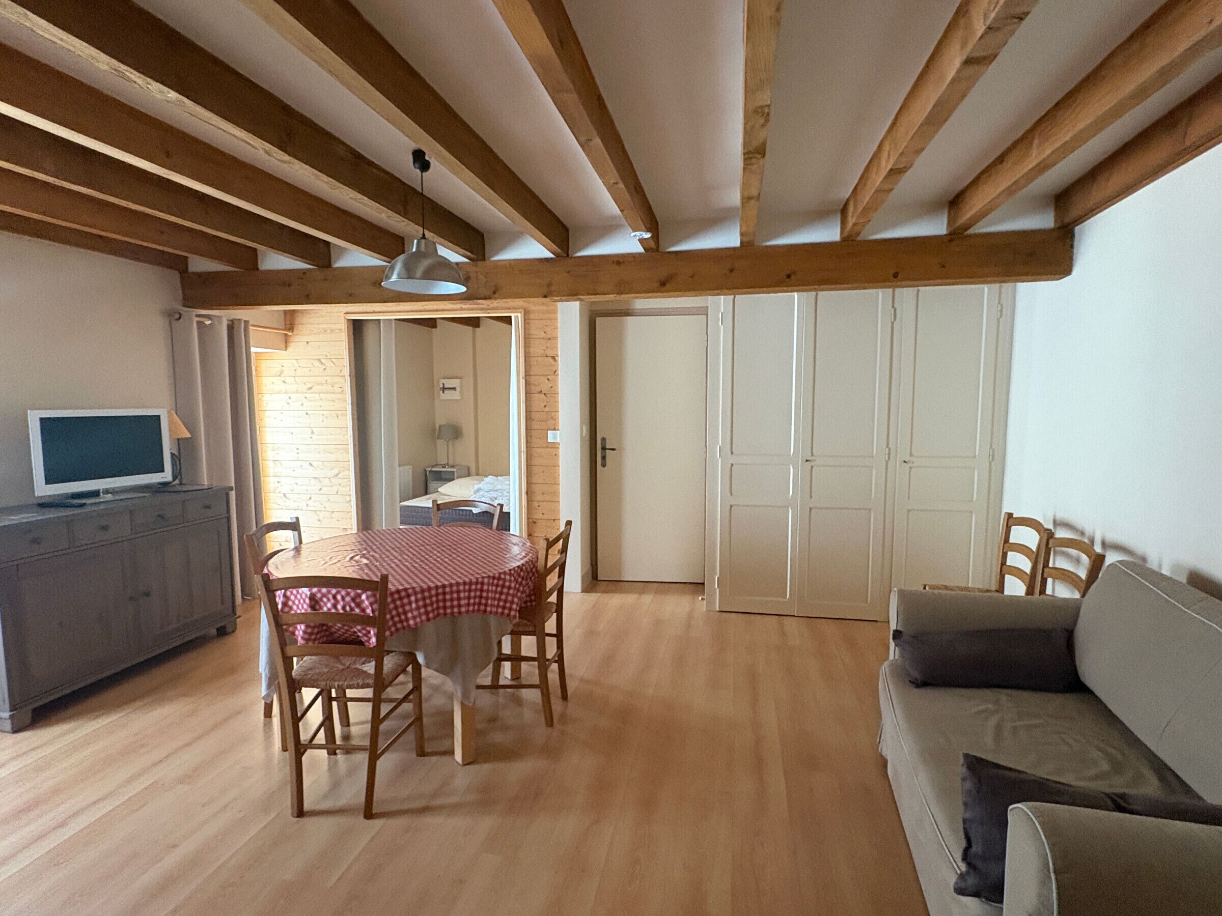 A cozy room with a wooden ceiling, a dining table with chairs, a sofa, and a TV on a cabinet.
