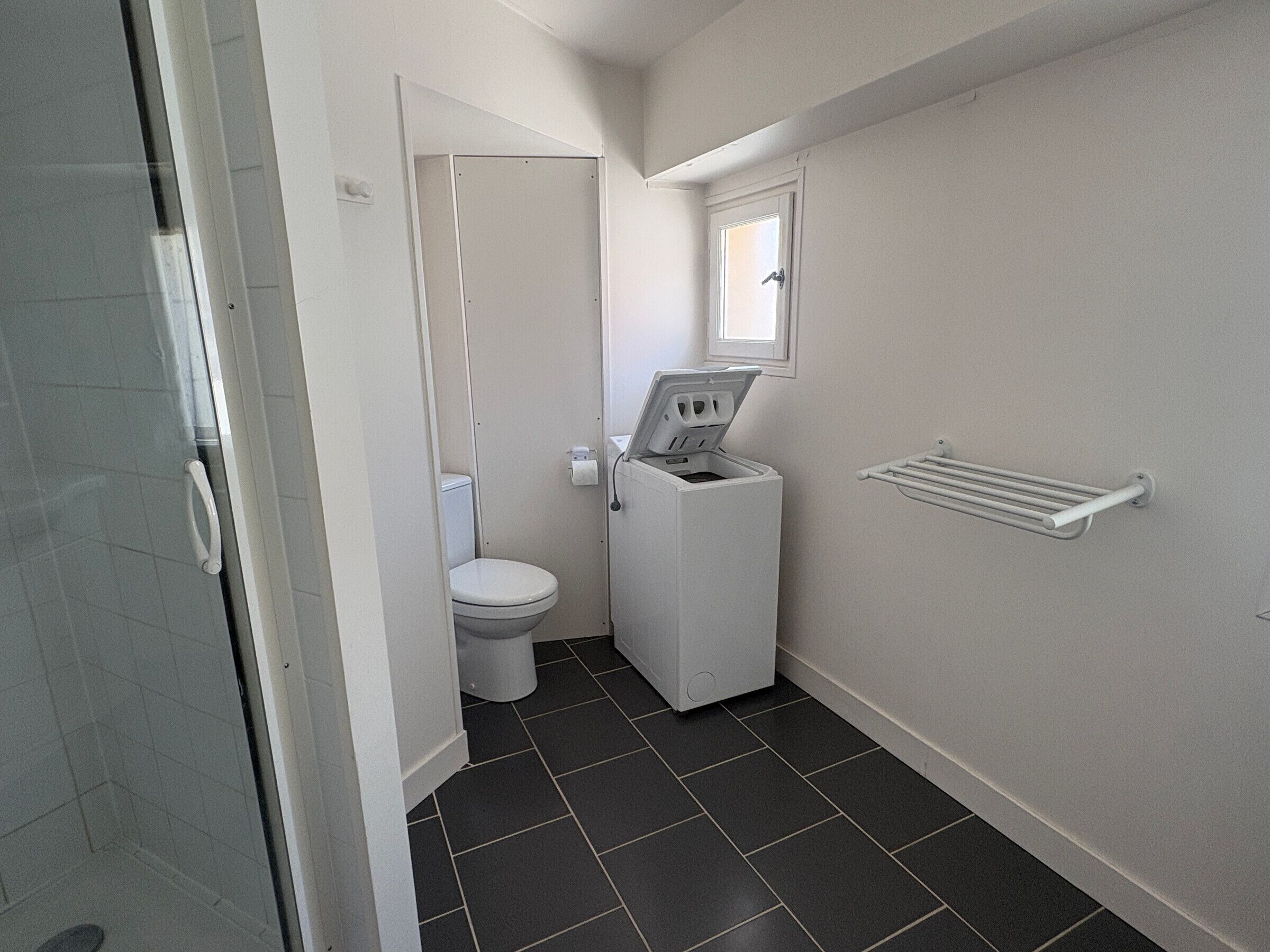A compact bathroom with a toilet, a washing machine, and a towel rack.