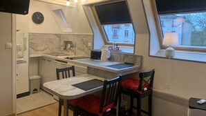A compact kitchen with a dining area, a TV mounted on the wall, and a clock.