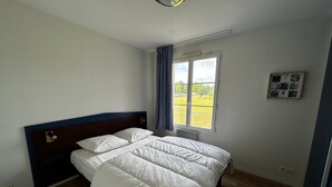 A bedroom with a bed, a window with curtains, and a wall-mounted picture. - T2 Apartment with Wi-Fi and Pool 200m from Spas (La Roche-Posay)