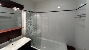 A modern bathroom with a glass shower enclosure, a white sink, and a mirror with a wooden frame. - T2 Apartment near Thermes with pool and WIFI (La Roche-Posay)