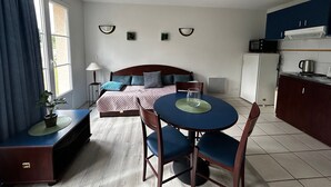 A compact hotel room with a bed, bedside table, lamp, and a small dining table with chairs. - T2 Apartment near Thermes with pool and WIFI (La Roche-Posay)