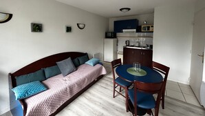 A compact living space with a sofa, a dining table with chairs, a kitchenette, and a small decorative plant. - T2 Apartment near Thermes with pool and WIFI (La Roche-Posay)