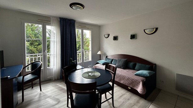 A room with a bed, a dining table with chairs, a window with curtains, and a ceiling light. - T2 Apartment near Thermes with pool and WIFI (La Roche-Posay)