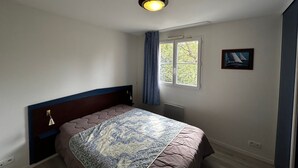 A bedroom with a bed, a window, a picture on the wall, and a ceiling light. - T2 Apartment near Thermes with pool and WIFI (La Roche-Posay)