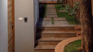 Een modern huis met een trap naar een houten deur, een kleine tuin en een boom.