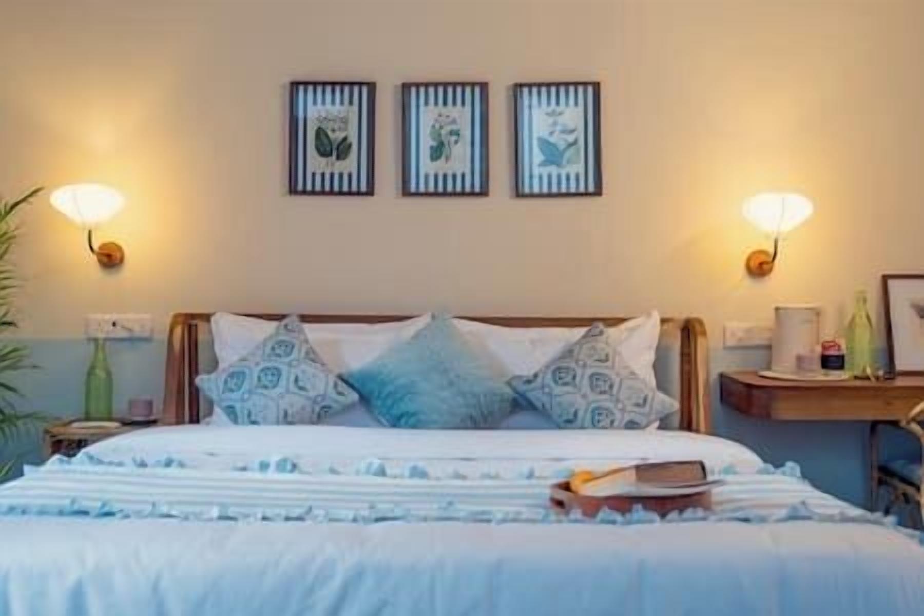 A neatly made bed with patterned pillows, a bedside table with a lamp, and wall-mounted artwork.