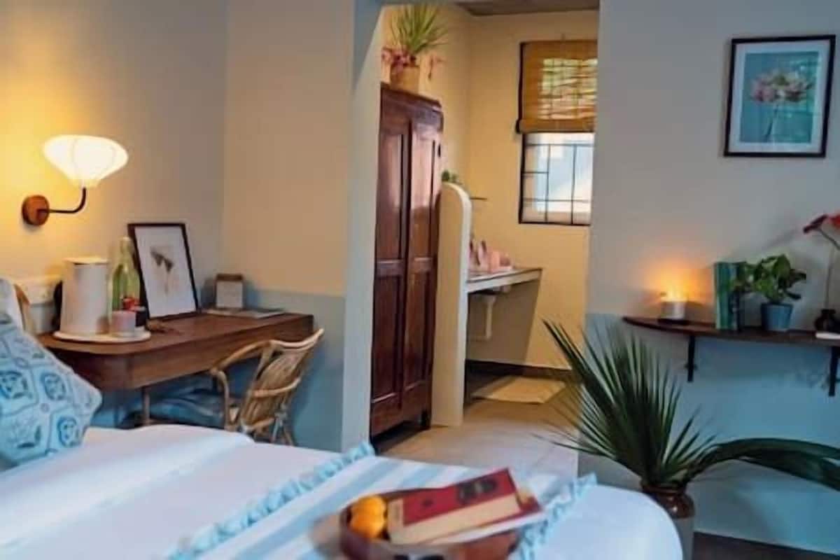A cozy bedroom with a bed, bedside table, lamp, and a desk with a chair.