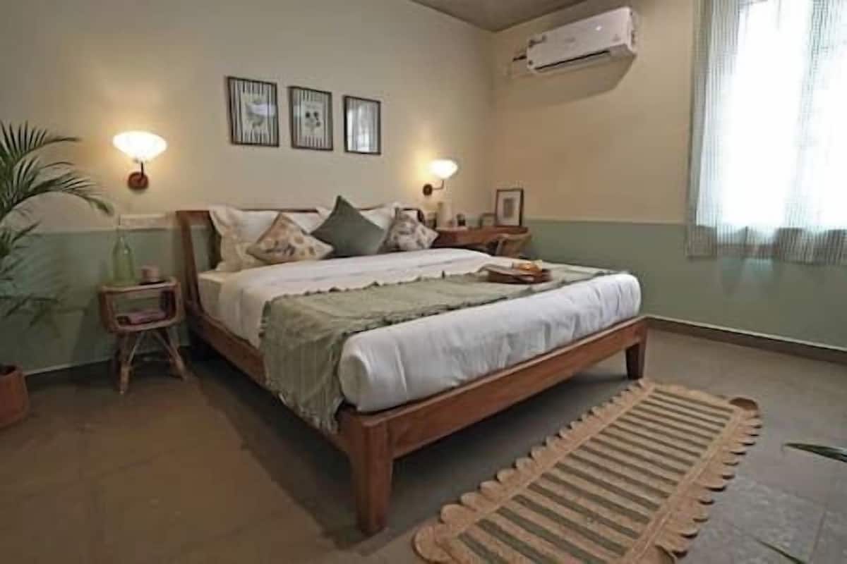 A bedroom with a wooden bed, two bedside tables, a nightstand, a floor lamp, and a wall-mounted air conditioner.