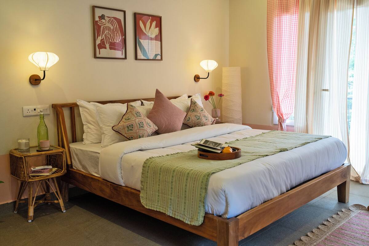 A neatly made bed with a wooden frame, a bedside table with a lamp, and a small wicker chair.