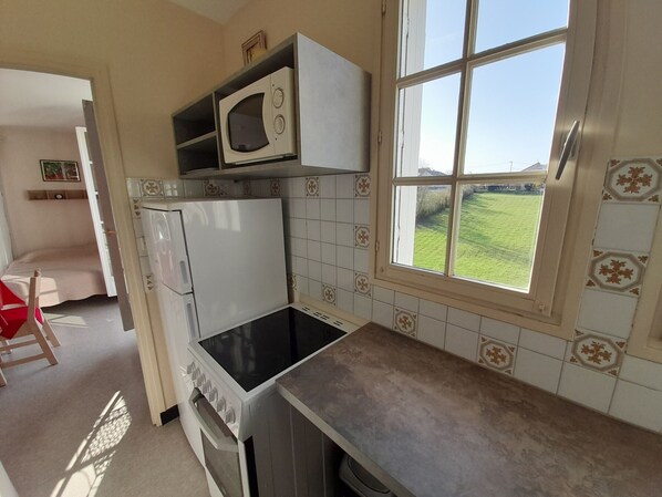 A compact kitchen with a microwave, stove, and a window with a view of a green field.