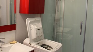 Ein Badezimmer mit Duschkabine aus Glas, einem weißen Waschbecken und einem roten Schrank.
