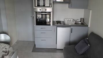Een kleine keuken met een inbouwoven, magnetron en koelkast.