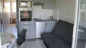 Uma cozinha compacta equipada com micro-ondas, forno e pia. Há um sofá e uma mesa de jantar com cadeiras.