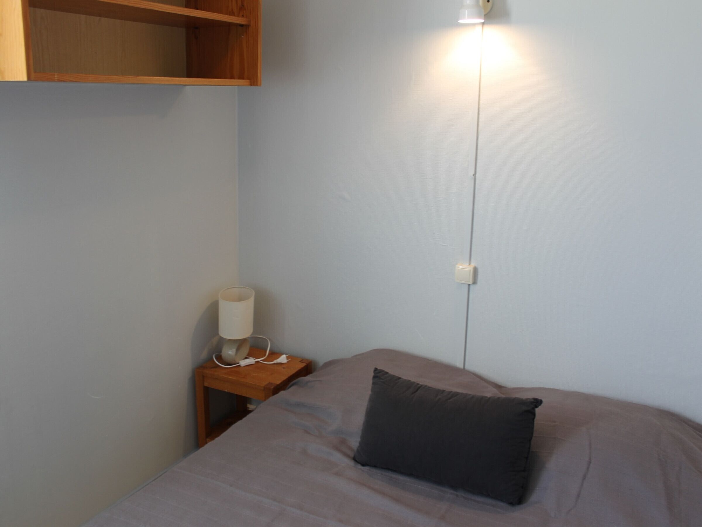 Een slaapkamer met een bed, nachtkastje, lamp en een stopcontact.