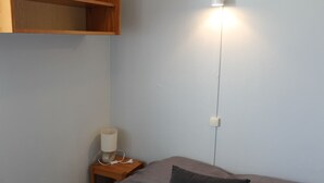 Quarto com cama, mesa de cabeceira, abajur e tomada na parede.