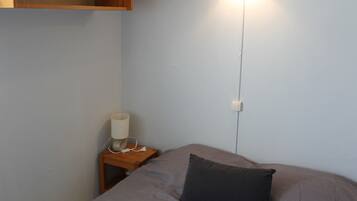 Een slaapkamer met een bed, nachtkastje, lamp en een stopcontact.