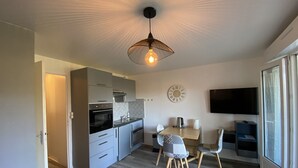 A modern kitchen with built-in appliances, a dining area with a wooden table and chairs, and a large window providing natural light. - 1-bedroom apartment with terrace and Wi-Fi near Connétable Thermal Baths (La Roche-Posay)