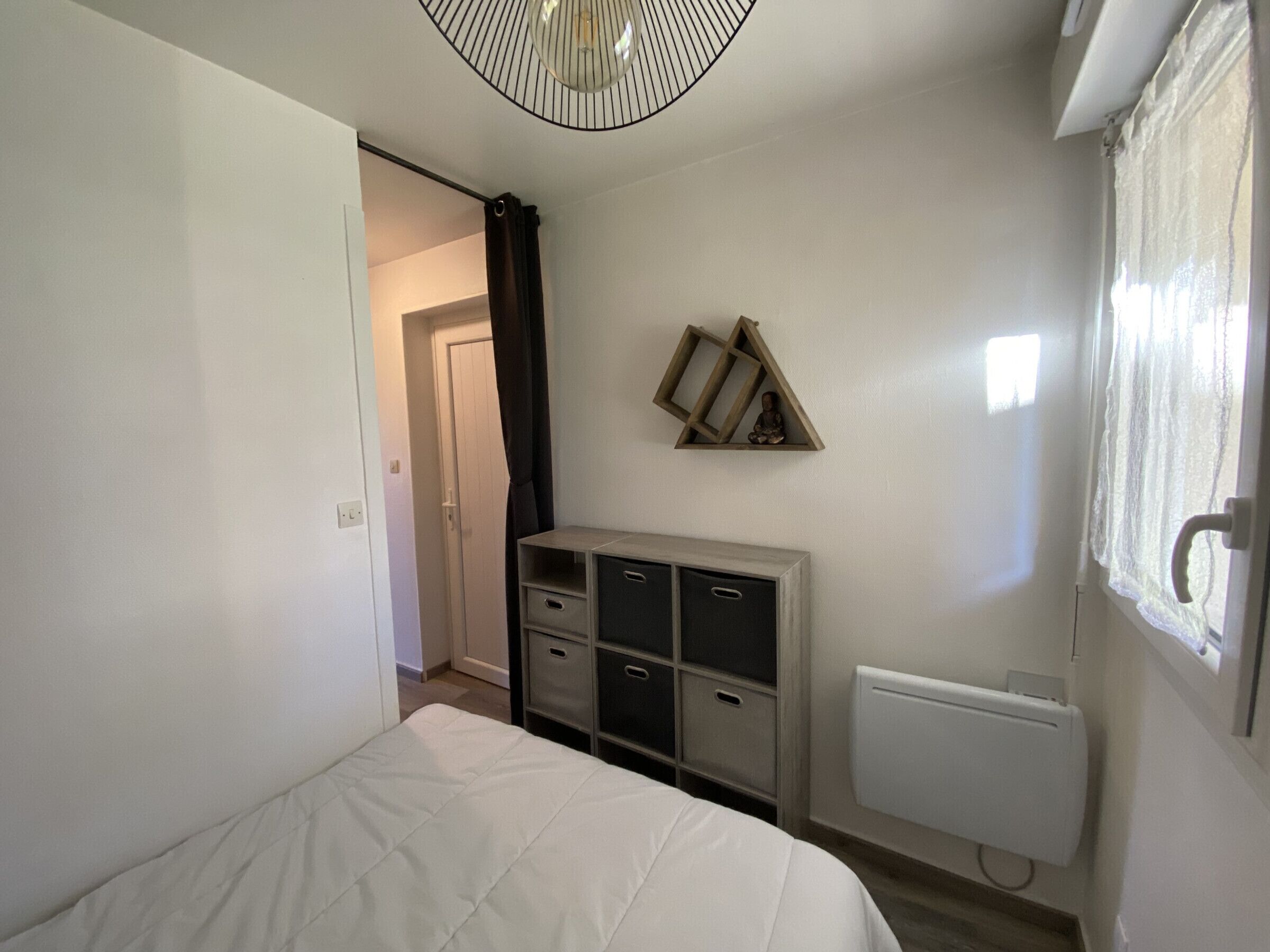 A bedroom with a bed, a dresser, a radiator, and a wall-mounted shelf with a statue.