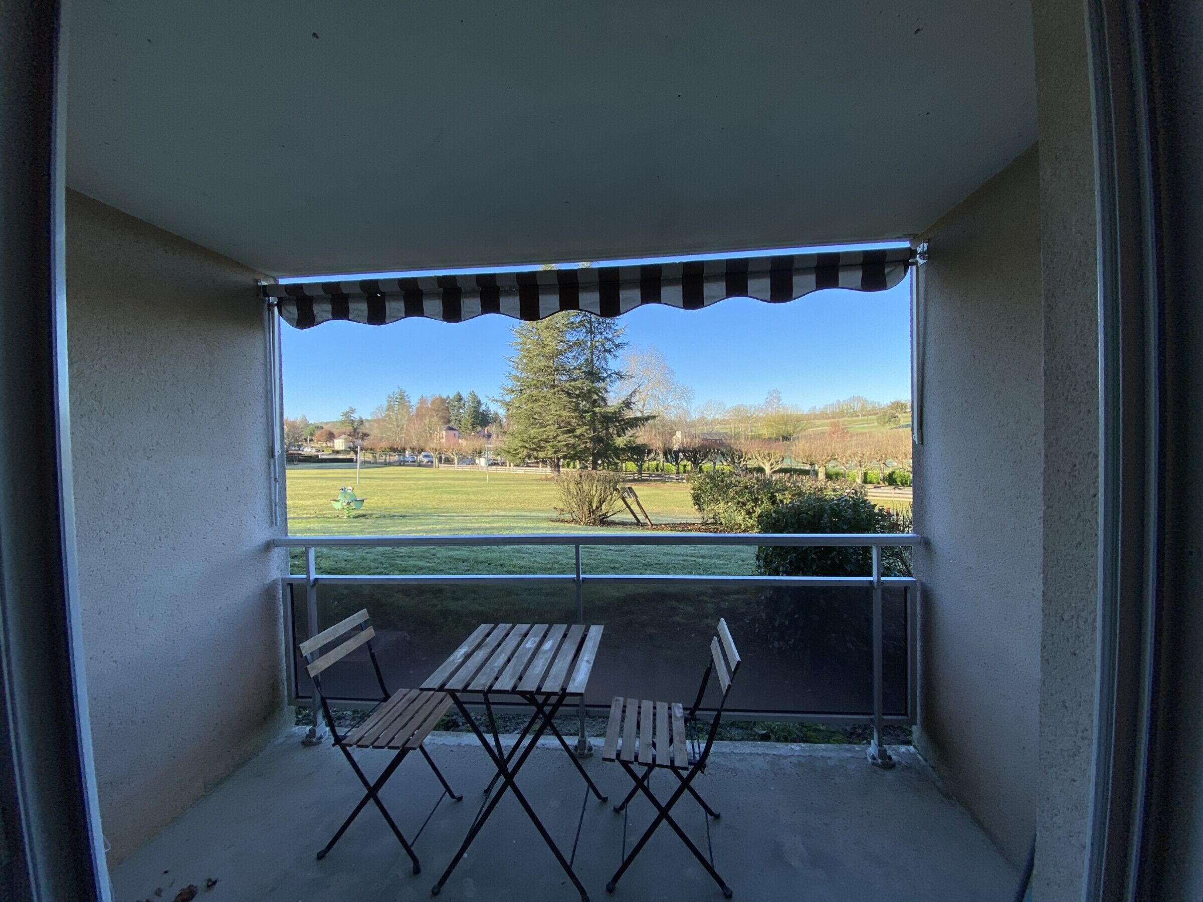 A balcony with a view of a green field and trees.
