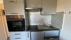 A compact kitchen with a built-in oven, a stainless steel sink, and a microwave. - 1-bedroom apartment with terrace and Wi-Fi near Connétable Thermal Baths (La Roche-Posay)