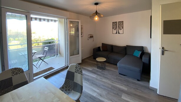 A living room with a sofa, a dining table, and chairs, a balcony with a table and chairs, and a ceiling light. - 1-bedroom apartment with terrace and Wi-Fi near Connétable Thermal Baths (La Roche-Posay)