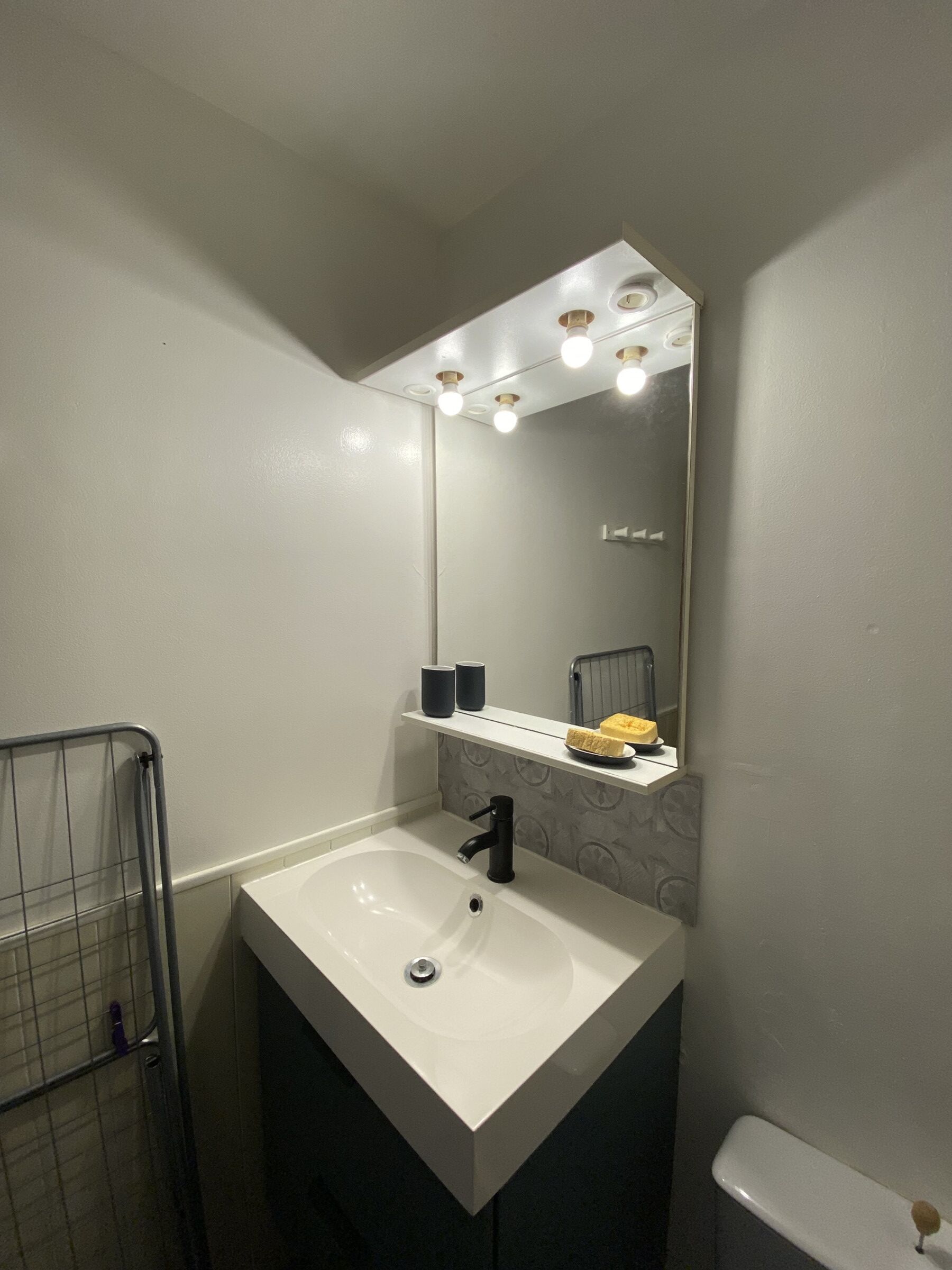A bathroom with a white sink, a mirror with lights, a towel rack, and a toilet.