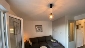A modern living room with a grey sectional sofa, a small round table, and a pendant light. - Charming T2 with terrace near Thermes du Connétable, Wi-Fi, dishwasher (La Roche-Posay)