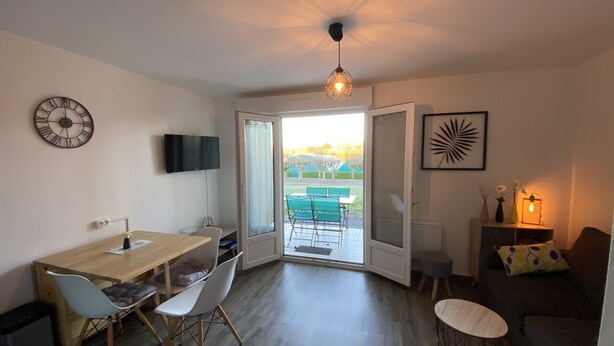 A modern living room with a dining area, a TV mounted on the wall, and a view of the outdoors. - Charming T2 with terrace near Thermes du Connétable, Wi-Fi, dishwasher (La Roche-Posay)