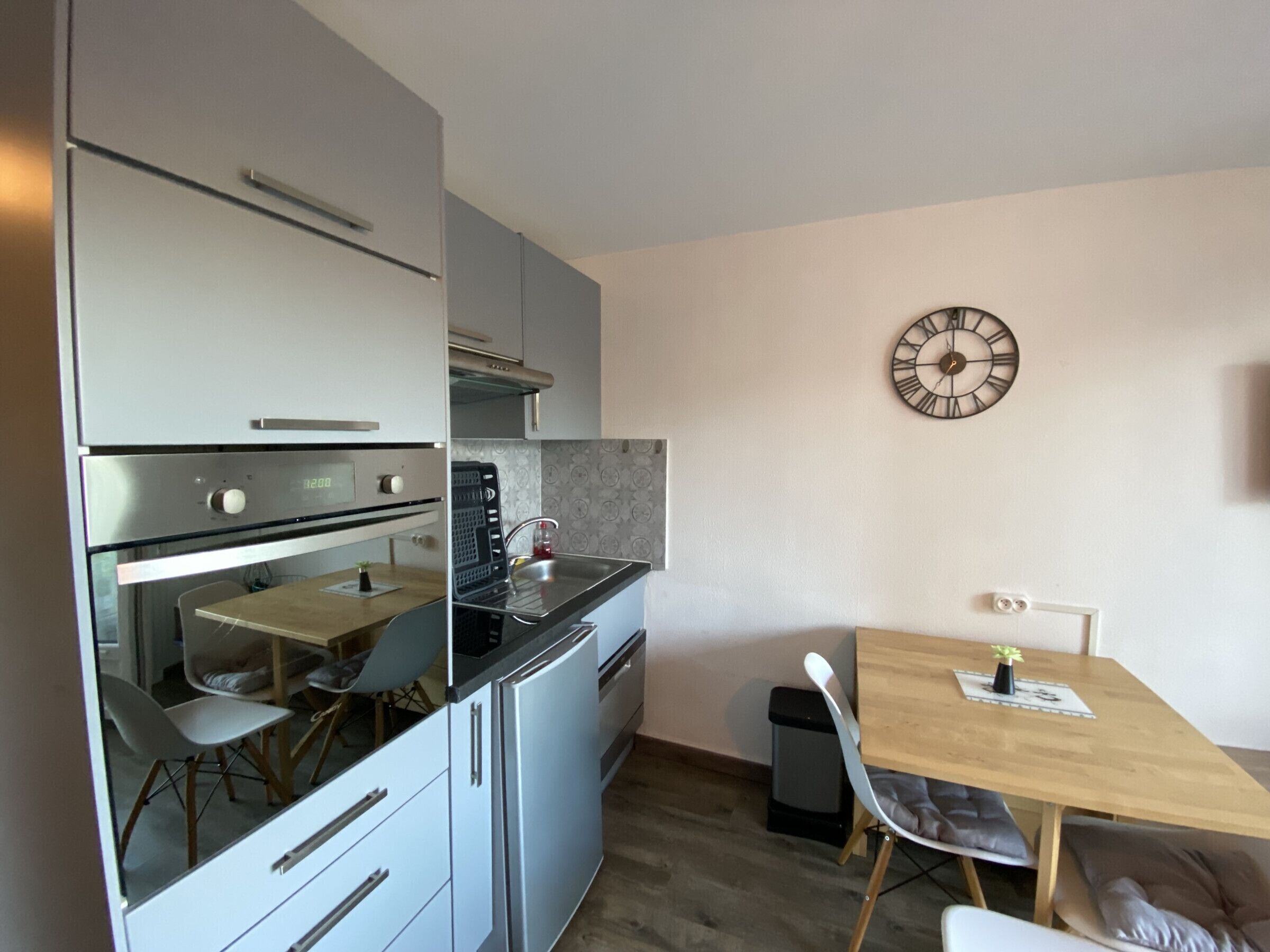 A compact kitchen with a built-in oven, a sink, and a dining area with a table and chairs.