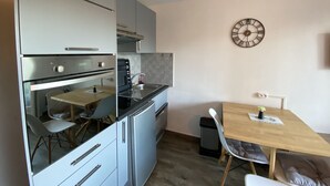 A compact kitchen with a built-in oven, a sink, and a dining area with a table and chairs. - Charming T2 with terrace near Thermes du Connétable, Wi-Fi, dishwasher (La Roche-Posay)