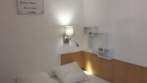 A minimalist hotel room with a wooden headboard, two white pillows, a bedside table, and a wall-mounted light fixture. - Charming T2 with terrace near Thermes du Connétable, Wi-Fi, dishwasher (La Roche-Posay)