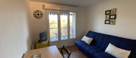 A living room with a wooden table, a blue sofa, and a TV on a small table.