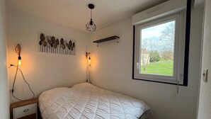 A bedroom with a bed, bedside table, wall-mounted light, and a window with a view of greenery. - 1-bedroom near Connétable Thermal Baths with balcony and Wi-Fi (La Roche-Posay)