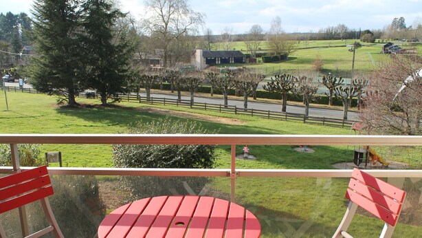 A balcony with a red table and chairs, overlooking a grassy area with trees and a building in the distance. - 1-bedroom near Connétable Thermal Baths with balcony and Wi-Fi (La Roche-Posay)