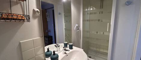 Un baño con lavamanos blanco, espejo y cabina de ducha de vidrio.