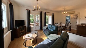 A living room with a sofa, a TV, a dining table, and a chandelier. - City center T3 apartment with garden and air conditioning (La Roche-Posay)