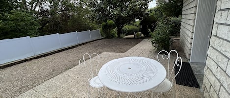 A patio with a round table and chairs, surrounded by a gravel area and a white fence.
