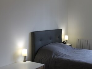 A bedroom with a large bed, two bedside tables, and a radiator. - Bright downtown T2 with Wi-Fi, washing machine and dishwasher (La Roche-Posay)