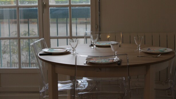 A dining table with clear glass chairs, a window with a view of the street, and a white tablecloth. - Bright downtown T2 with Wi-Fi, washing machine and dishwasher (La Roche-Posay)