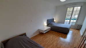 A room with two beds, a bedside table, a nightstand, and a window with a view of the outside. - Bright downtown T2 with Wi-Fi, washing machine and dishwasher (La Roche-Posay)