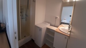 A bathroom with a glass-enclosed shower, a white washing machine, and a sink with a mirror. - Bright downtown T2 with Wi-Fi, washing machine and dishwasher (La Roche-Posay)