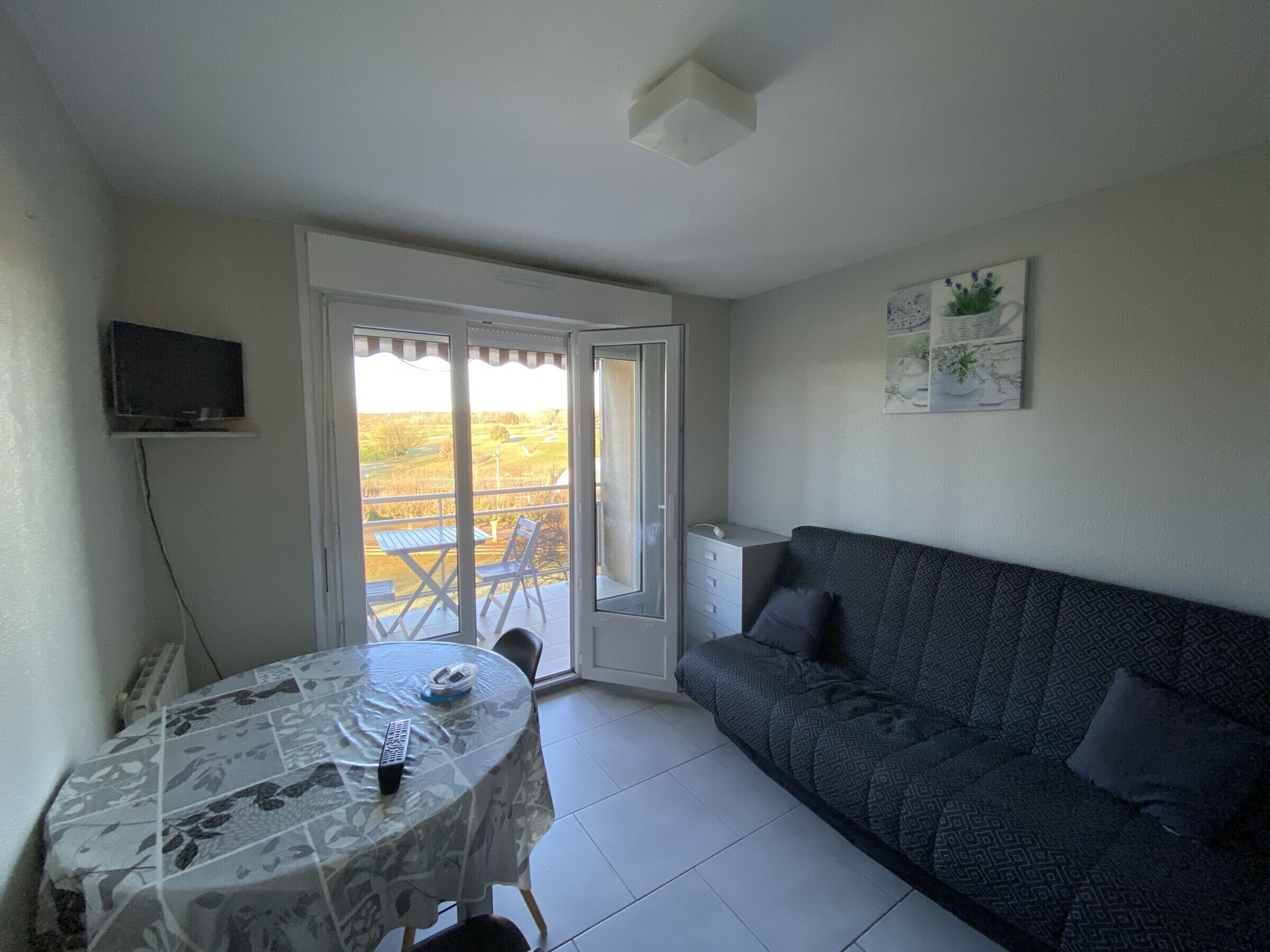 Une pièce comprenant une table à manger, un canapé, un téléviseur fixé au mur et une porte-fenêtre coulissante donnant sur un espace extérieur.
