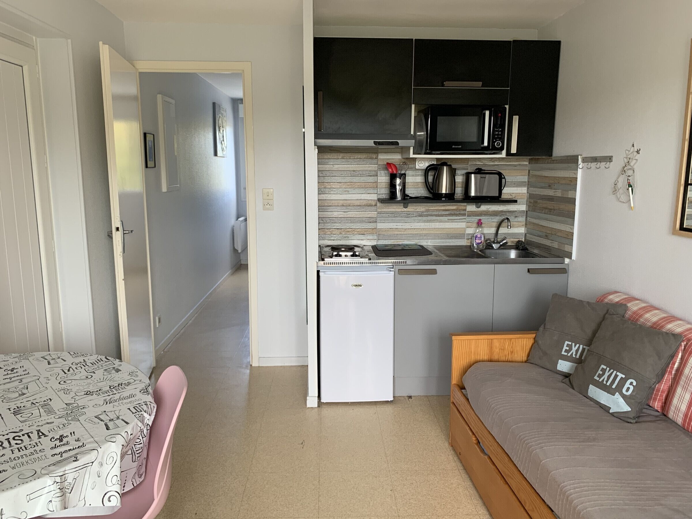 Cocina compacta con microondas, hervidor, cafetera, refrigerador pequeño y sofá con almohada con señal de salida.